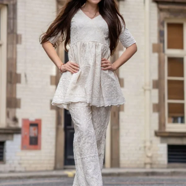 Woman wearing an elegant white pure cotton kurta and pant set featuring delicate chikankari and sequin embroidery – stylish and breathable readymade suit for women.